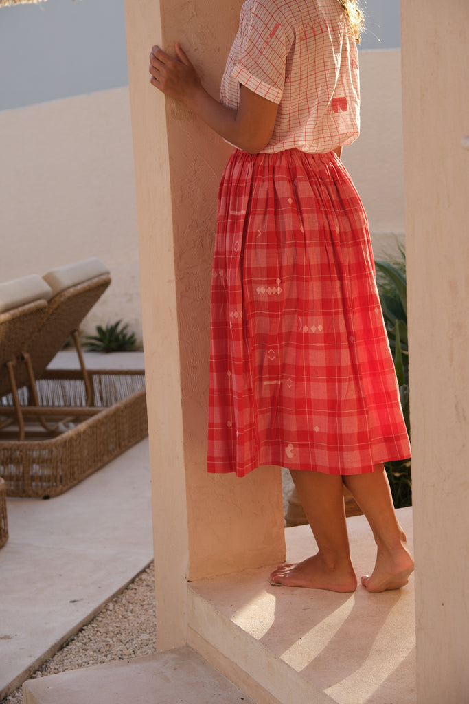 Presenting the Crimson Checkered Cuban Shirt, a joint creation by Audrey E Leary and World of Crow. This shirt, crafted from delicately hand-woven jamdani fabric, features a soft pink hue adorned with red patterns. With its short sleeves and airy, lightweight design, it’s ideal for daily wear. Sustainably produced from plush cotton, it pairs beautifully with a red checkered skirt