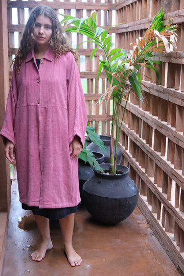 Presenting the Duster Jacket in a charming pink, crafted from premium handwoven organic cotton by Audrey E Leary and World of Crow. It features a straight collar, coconut buttons, and a relaxed fit with a straight hem. Offering a comfortable, midweight feel and true-to-size fit, this versatile jacket is perfect for enhancing both formal and casual outfits