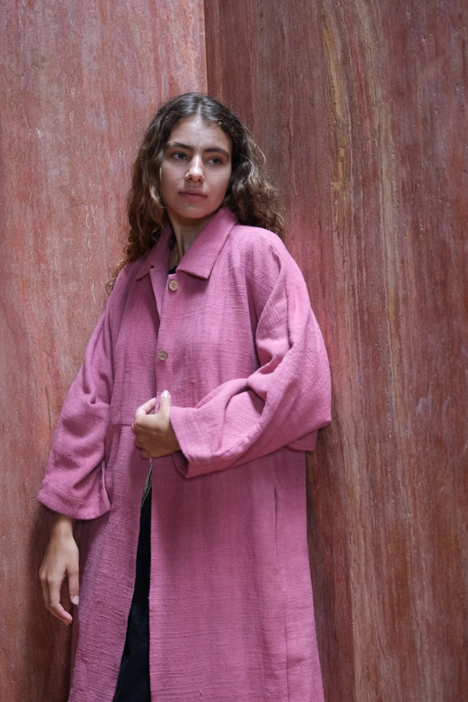 Presenting the Duster Jacket in a charming pink, crafted from premium handwoven organic cotton by Audrey E Leary and World of Crow. It features a straight collar, coconut buttons, and a relaxed fit with a straight hem. Offering a comfortable, midweight feel and true-to-size fit, this versatile jacket is perfect for enhancing both formal and casual outfits