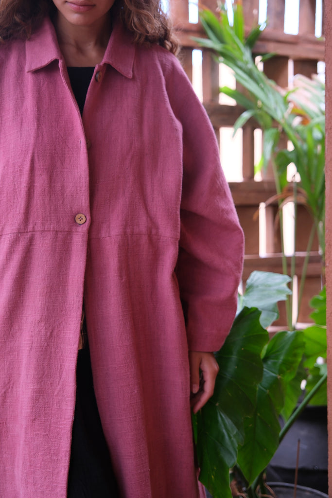 Presenting the Duster Jacket in a charming pink, crafted from premium handwoven organic cotton by Audrey E Leary and World of Crow. It features a straight collar, coconut buttons, and a relaxed fit with a straight hem. Offering a comfortable, midweight feel and true-to-size fit, this versatile jacket is perfect for enhancing both formal and casual outfits