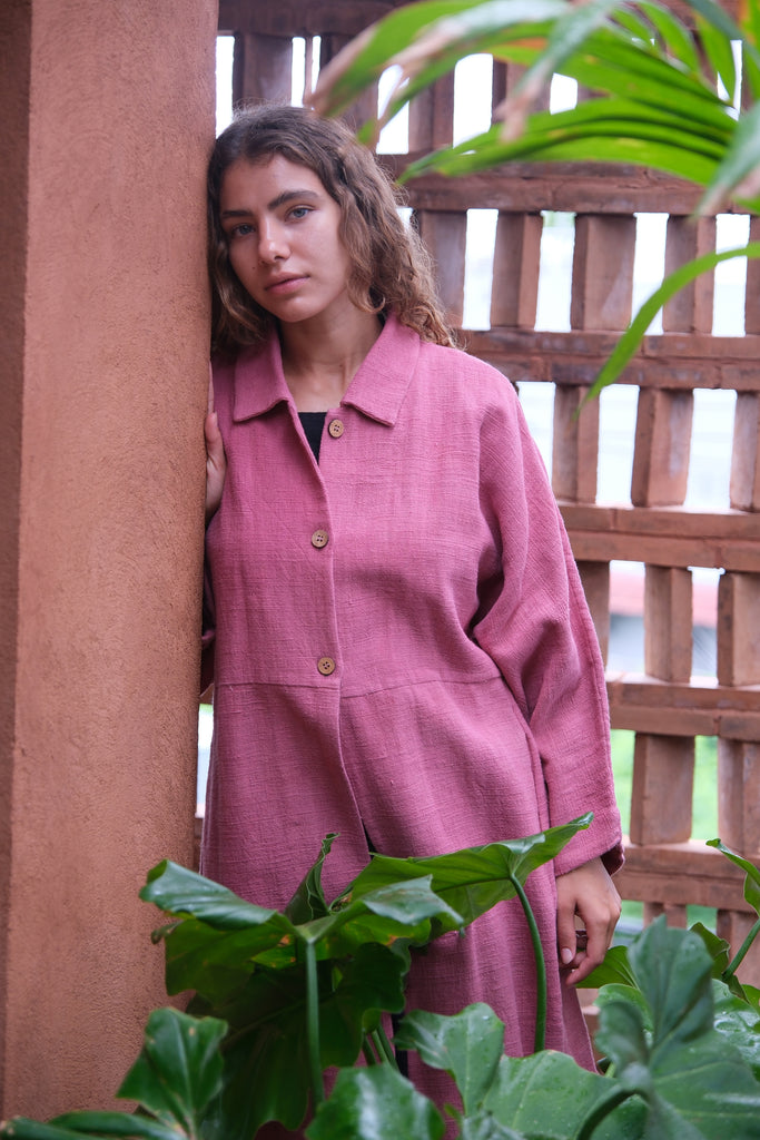 Presenting the Duster Jacket in a charming pink, crafted from premium handwoven organic cotton by Audrey E Leary and World of Crow. It features a straight collar, coconut buttons, and a relaxed fit with a straight hem. Offering a comfortable, midweight feel and true-to-size fit, this versatile jacket is perfect for enhancing both formal and casual outfits