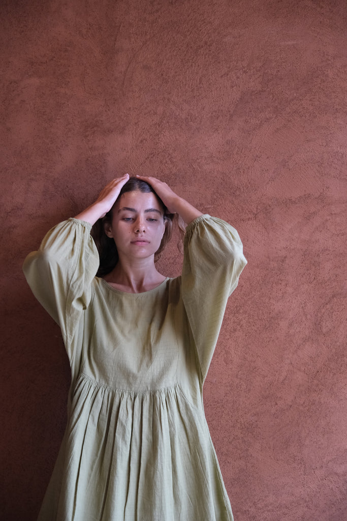 Presenting the Olive Get Away Dress, a collaboration between Audrey E Leary and World of Crow. This unique olive green mini dress features a scoop neckline, three-quarter puff sleeves, and is made from soft, handwoven cotton, offering a breathable, comfortable fit ideal for daily wear.