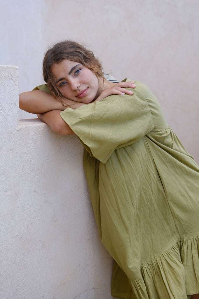 Presenting the Olive Green Day Dress, a collaboration between Audrey E Leary and World of Crow. This mini dress features a V-neck, drop shoulders, and a distinctive olive green shade. Crafted from soft, handwoven cotton, it provides a comfortable, lightweight fit ideal for daily wear.