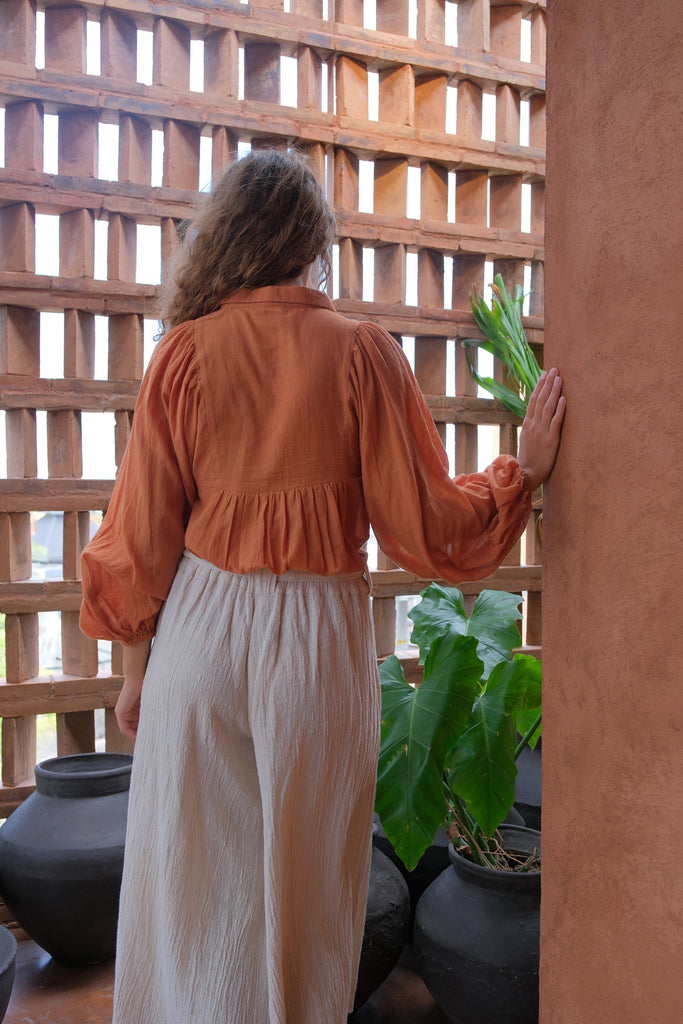 Presenting the Audrey X Crow Collection, featuring a woman in an orange Jane Austen Shirt and a white skirt. Showcasing handwoven fabric with block-printed stripes, this collection combines vibrant orange with classic white for an elegant and sophisticated look.