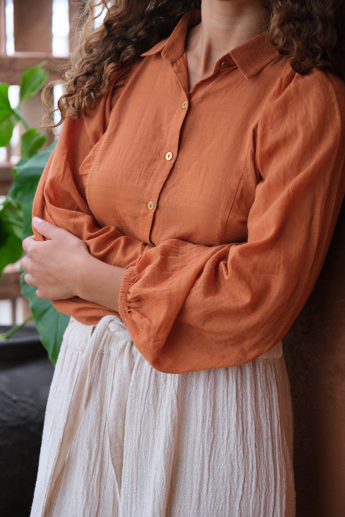 Presenting the Audrey X Crow Collection, featuring a woman in an orange Jane Austen Shirt and a white skirt. Showcasing handwoven fabric with block-printed stripes, this collection combines vibrant orange with classic white for an elegant and sophisticated look.