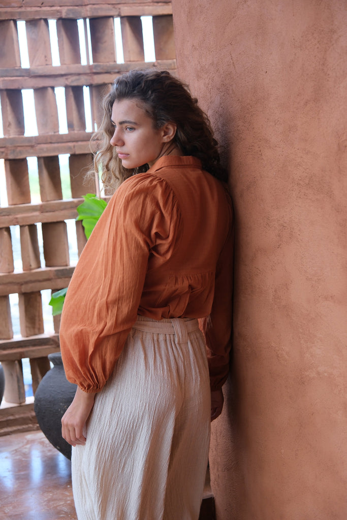 Presenting the Audrey X Crow Collection, featuring a woman in an orange Jane Austen Shirt and a white skirt. Showcasing handwoven fabric with block-printed stripes, this collection combines vibrant orange with classic white for an elegant and sophisticated look.