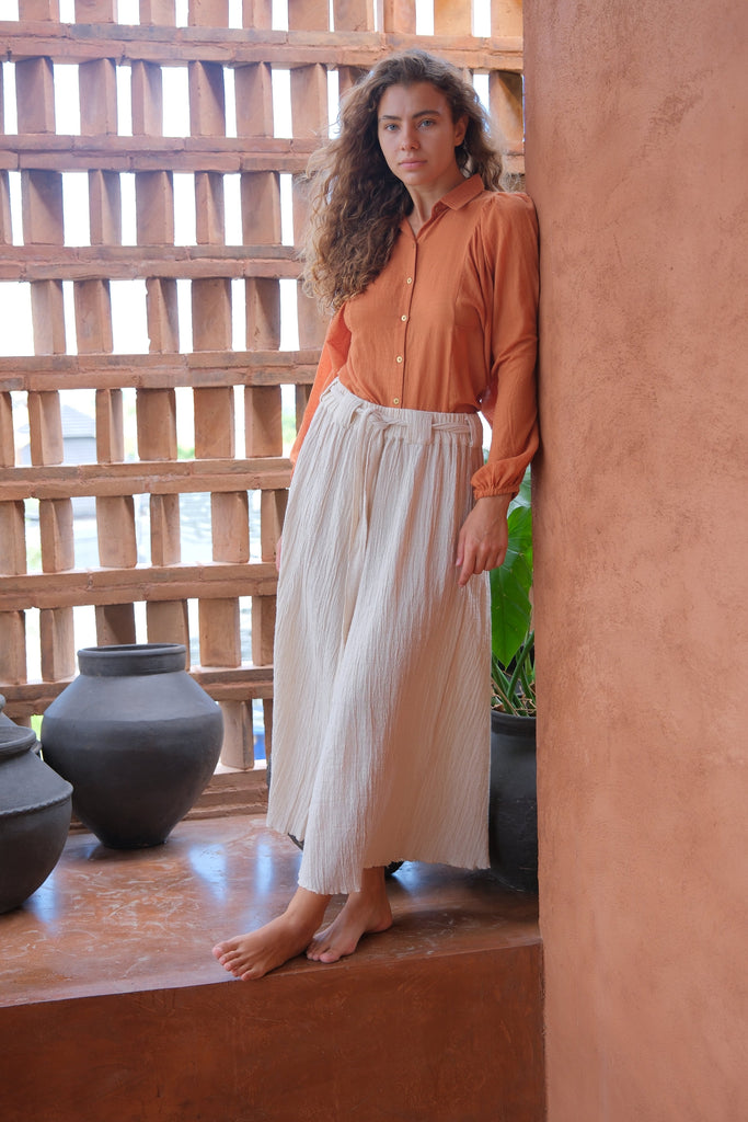 Presenting the Audrey X Crow Collection, featuring a woman in an orange Jane Austen Shirt and a white skirt. Showcasing handwoven fabric with block-printed stripes, this collection combines vibrant orange with classic white for an elegant and sophisticated look.