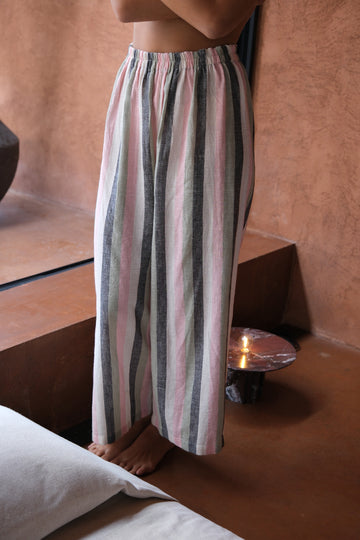 Presenting Boatman’s Pants, crafted from handwoven organic cotton and featured on a woman standing by a bed. Combining comfort with style, these pants showcase artisanal quality and offer a sustainable, elegant choice for any occasion.