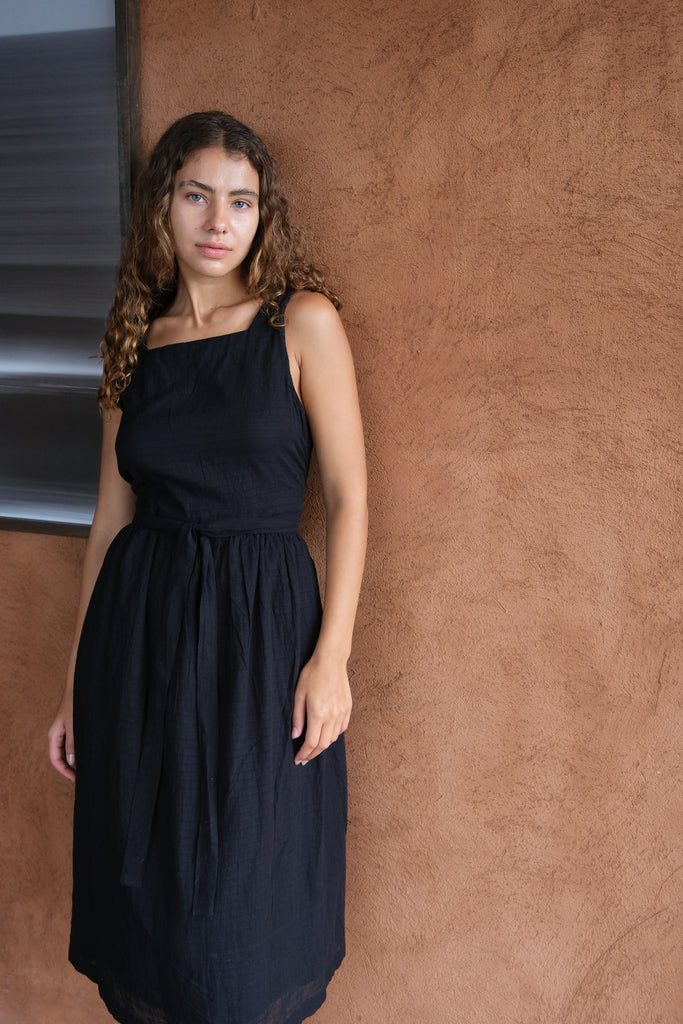 Presenting The Classic Hitch Dress, a sleek collaboration between Audrey E Leary and World of Crow. This black midi dress features a square neckline, wrap-around design with a drawstring waist, and a comfortable, true-to-size fit in soft, lightweight fabric.