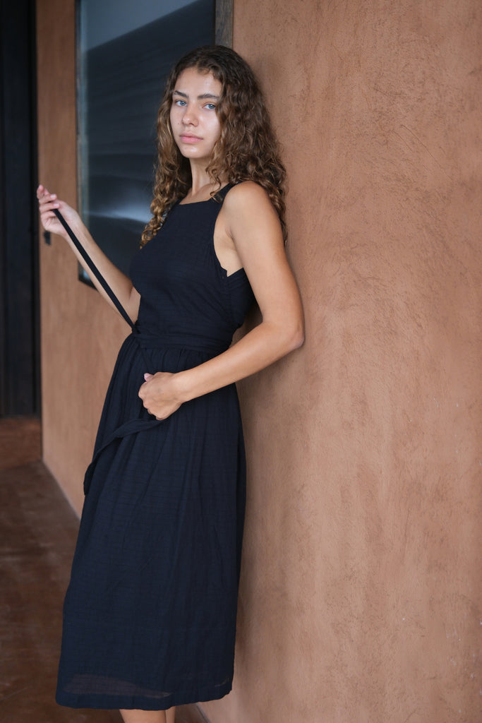 Presenting The Classic Hitch Dress, a sleek collaboration between Audrey E Leary and World of Crow. This black midi dress features a square neckline, wrap-around design with a drawstring waist, and a comfortable, true-to-size fit in soft, lightweight fabric.